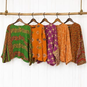 May include: Five long-sleeved shirts hanging on wooden hangers from a horizontal wooden rod. The shirts feature various patterns and colours, including green with paisley, orange with geometric shapes, purple with grid lines, and solid orange and brown.