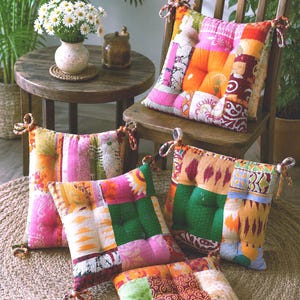 May include: Four square seat cushions featuring a patchwork design with various colorful fabric patterns including pink, orange, green, and yellow. Each cushion has tufted centers and fabric ties at the corners for securing to chair frames.