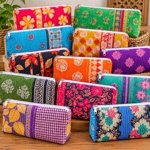 May include: A collection of rectangular zipped pouches made from quilted fabric in various vibrant colours and patterns, including floral, geometric, and paisley prints. Each pouch features a white zip closure along the top edge.