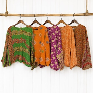 Könnte beinhalten: Fünf langärmelige Hemden hängen an Holzkleiderbügeln an einer horizontalen Holzstange. Die Hemden weisen verschiedene Muster und Farben auf, darunter Grün mit Paisley-Mustern, Orange mit geometrischen Formen, Violett mit Linien sowie Orange und Braun.