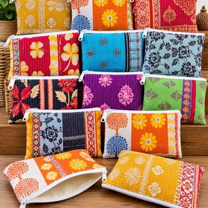 Op de afbeelding: Een collectie rechthoekige stoffen tasjes met diverse kleurrijke bloemen- en boompatronen en witte ritsen. Elk klein tasje toont verschillende doorgestikte texturen en levendige prints in tinten geel, rood, blauw, paars en groen.
