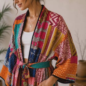 Könnte beinhalten: Ein Kimono-Bademantel im Patchwork-Design mit einer lebendigen Mischung aus Blumen-, geometrischen und Karomustern in Magenta, Orange, Petrol und Blau. Das Kleidungsstück verfügt über einen schwarzen Saum, weite Ärmel, einen Bindegürtel.