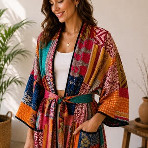 Könnte beinhalten: Ein langärmeliger Morgenmantel mit einem lebendigen Patchwork-Design aus verschiedenen Blumen- und geometrischen Mustern in Rot-, Orange-, Blau- und Gelbtönen. Das Kleidungsstück verfügt über einen passenden Bindegürtel, zwei Vordertaschen und einen schwarzen Saum.