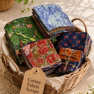 May include: A woven wicker basket filled with stacks of assorted cotton fabric scraps featuring various floral patterns in green, blue, red, and orange. A brown paper tag attached to the basket displays the text Cotton Fabric Scraps.
