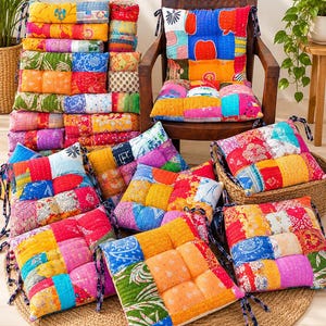 May include: A collection of square, tufted floor cushions featuring a patchwork design of various colorful fabrics with intricate patterns. Each cushion includes fabric ties at the corners and visible stitching throughout the quilted surface.