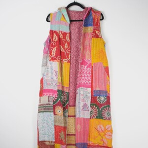 Puede incluir: Un chaleco sin mangas con capucha y largo hasta la rodilla que presenta un vibrante diseño de patchwork. La prenda está confeccionada con varios paneles de tela en tonos brillantes de amarillo, rojo, rosa, verde y azul, con diversos patrones florales.