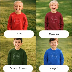 Peut inclure: Quatre sweat-shirts pour enfants, rouges, marron, vert for&ecirc;t et bleu roi. Chaque sweat-shirt porte un logo circulaire blanc avec le texte "Little Marks". Les enfants sourient et se tiennent sur l'herbe.