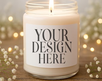 May include: A lit candle in a clear glass jar with a white label that reads "YOUR DESIGN HERE." The candle is surrounded by fairy lights and small white flowers, set on a wooden surface.