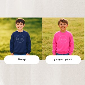 Peut inclure: Deux enfants portant des sweatshirts. L'un porte un sweat-shirt bleu marine, l'autre un rose vif. Chaque sweat-shirt pr&eacute;sente un motif circulaire blanc avec le texte "Little Whales". L'arri&egrave;re-plan est un champ herbeux. V&ecirc;tements pour enfants.