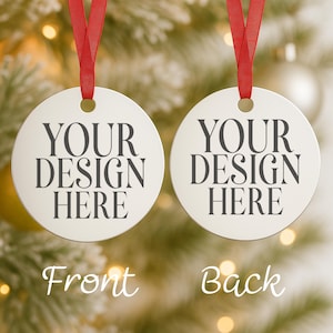 Pode incluir: Dois enfeites de Natal redondos e brancos com fitas vermelhas. Cada enfeite tem o texto "YOUR DESIGN HERE" em preto. Um enfeite está rotulado "Front" e o outro "Back". O fundo é uma imagem desfocada de uma árvore de Natal.