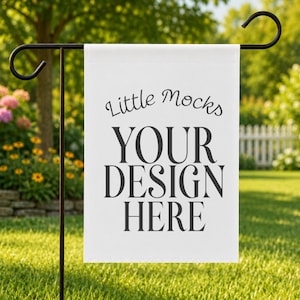 May include: A white garden flag with the text "Little Mocks YOUR DESIGN HERE" in black. The flag is hanging on a black metal stand in a grassy yard with flowers and trees in the background.