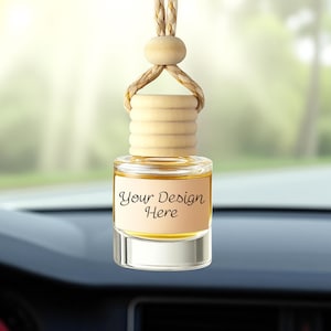 Puede incluir: Un ambientador para coche con un frasco de vidrio transparente que contiene un líquido ámbar claro. El frasco tiene una tapa de madera y una etiqueta beige con el texto "Your Design Here". Una cuerda trenzada está unida para colgar.