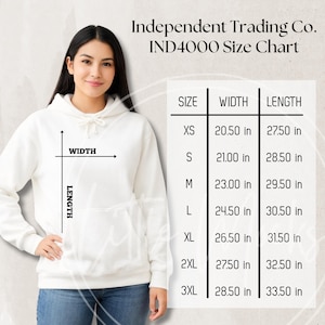 Puede incluir: Una mujer con una sudadera blanca, con una tabla de tallas para el modelo IND4000 de Independent Trading Co. La tabla muestra medidas de ancho y largo en cm, desde la XS hasta la 3XL.
