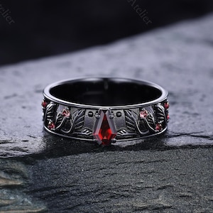 May include: A black ring with a central red gemstone and decorative floral and leaf patterns. The ring features small red accents and is set against a dark background. The Freya Atelier is printed on the top right.
