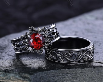 May include: Two black rings, one with a heart-shaped red gemstone and floral detailing, the other with a matching floral pattern. The rings are displayed on a dark, textured surface, showcasing their intricate design and gothic aesthetic.