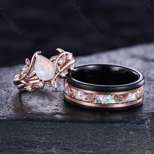 May include: A rose gold engagement ring with a pear-shaped opal center stone and a matching black band ring with opal and rose gold accents. The engagement ring features a leaf and vine design with small accent stones.