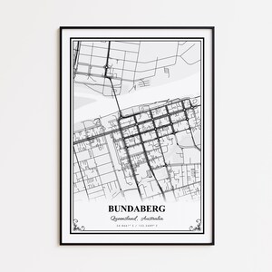 May include: A framed black and white map print of Bundaberg, Queensland, Australia. The map features a detailed street grid and is labeled with the city's name and coordinates. The print is enclosed in a black frame with decorative corner accents.