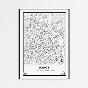 May include: A framed black and white map print of Nancy, France. The map details the city's layout, with streets and buildings depicted in fine lines. The city's name and coordinates are printed at the bottom.