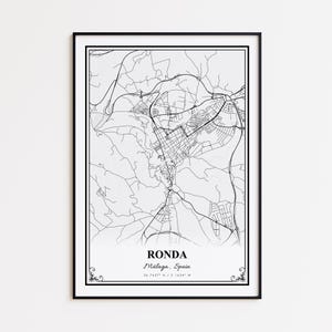May include: A framed black and white map print of Ronda, Málaga, Spain. The map details the city's streets and surrounding areas. The city name and coordinates are printed at the bottom. The print is in a black frame.