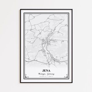 May include: A framed black and white map print of Jena, Thuringia, Germany. The map features detailed road and building outlines, with the city name and coordinates at the bottom. The print is encased in a black frame with decorative corner accents.