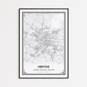 May include: A framed black and white map print of Odense, Denmark. The map shows the city's road network and is labeled with the city name, region, and coordinates. The print has a black border and decorative flourishes.