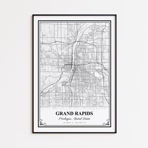May include: A framed black and white map print of Grand Rapids, Michigan, USA. The map shows the city's streets and waterways. The city name and coordinates are printed at the bottom of the map.