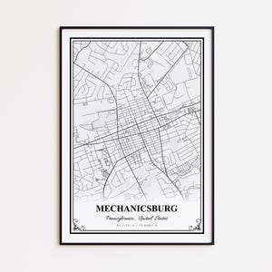 May include: A framed black and white map print of Mechanicsburg, Pennsylvania, United States. The map features a detailed street layout, with the town's name and coordinates displayed below. The print is encased in a black frame.