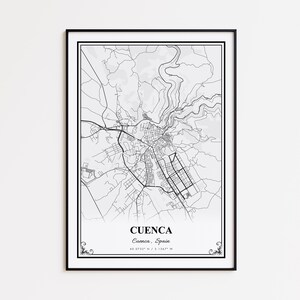 May include: A framed black and white map print of Cuenca, Spain. The map details the city's layout, including roads, buildings, and the surrounding terrain. The city's name and coordinates are printed at the bottom.