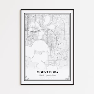 May include: A framed black and white map print of Mount Dora, Florida, United States. The map details the city's layout, including roads and bodies of water. The city name and coordinates are printed at the bottom.