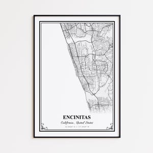 May include: A framed black and white map print of Encinitas, California, USA. The map shows the city's streets and topography. The city name and coordinates are printed at the bottom. The frame is black with decorative corner accents.
