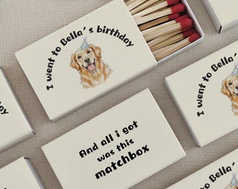 May include: Several white matchboxes with text and a Golden Retriever illustration. One box is open, revealing wooden matches with red tips. The text reads "I went to Bella's birthday" and "And all I got was this matchbox."
