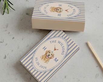 May include: Two matchboxes with a light blue and white striped design. Each box features a watercolor illustration of a golden retriever, the text "THE WILSONS", initials, and a date. Two matches with red tips are also visible.
