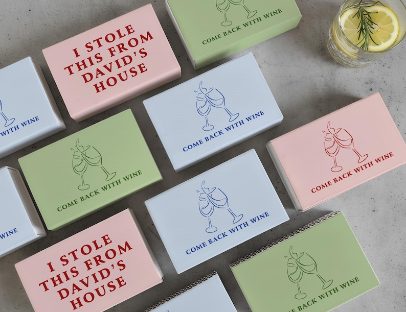 May include: A collection of small, rectangular boxes in various colors, including pink, green, and white. Some boxes feature the text "I STOLE THIS FROM DAVID'S HOUSE" in red. Other boxes have wine glass illustrations and the phrase "COME BACK WITH WINE."