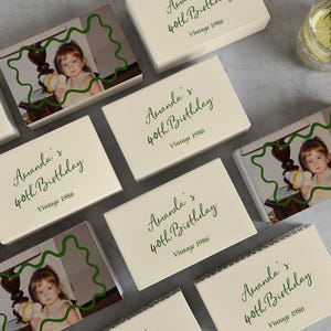 May include: A white ceramic mug with a black handle and the text "But First, Coffee" in a bold, black font. The mug is set against a blurred background, suggesting a cozy setting. The mug appears to be approximately 4 inches tall.