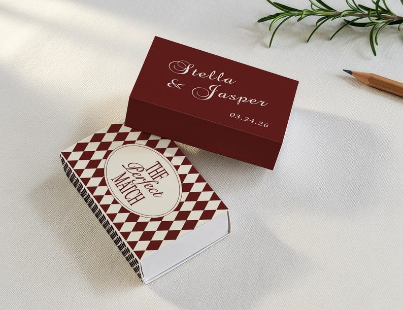 May include: Two decorative matchboxes. One is burgundy with the names "Stella & Jasper" and a date in white script. The other has a diamond pattern in burgundy and white, with the text "The Perfect Match" in an oval.