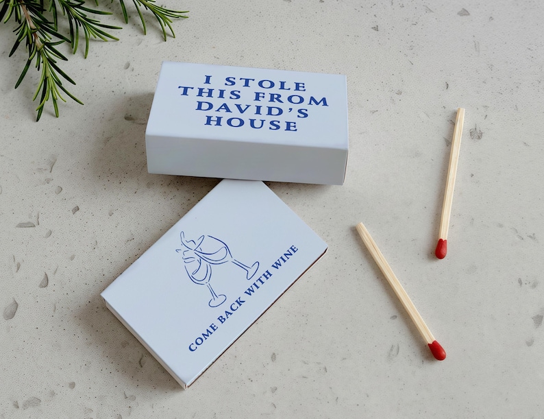 May include: Two white matchboxes with blue text and a wine glass design. One box reads "I STOLE THIS FROM DAVID'S HOUSE." The other says "COME BACK WITH WINE." Two matches with red tips are also visible.