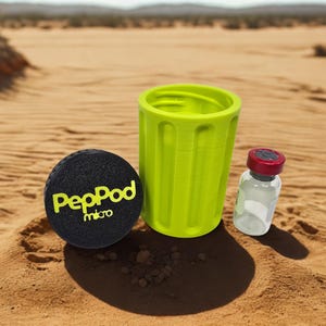 May include: A black, round PepPod micro device with yellow text, a lime green cup, and a small glass vial with a red cap. The items are set on a sandy surface with a desert backdrop.