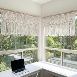 May include: Two off-white macrame window valances featuring a knotted leaf and vine pattern. Each valance hangs from a wooden rod and consists of vertical cord strands with small knotted ends, creating a textured fringe across the window.