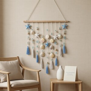 May include: A wall hanging featuring a horizontal wooden rod with white cords suspended from it. The cords are adorned with light blue and white starfish, various seashells, small turquoise and wooden beads, and light blue and white tassels.