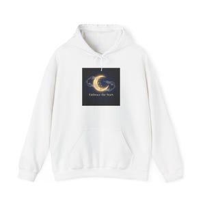 Peut inclure: Un sweat à capuche blanc avec une poche avant. Le sweat-shirt présente un graphisme d'un croissant de lune et de nuages avec le texte "Embrace the Stars" sur le devant. Le sweat à capuche est fait d'une matière douce.