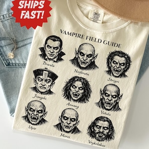 May include: An ivory t-shirt featuring a black graphic print titled Vampire Field Guide. The design displays nine detailed illustrations of various vampire figures, each labeled with their name, including Dracula, Nosferatu, and Strigoi.