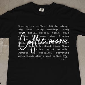 May include: Black t-shirt with white text. The shirt features the words "Coffee Mom" in a cursive font, with a list of coffee-related phrases. The shirt is a crew neck and made of a soft material.