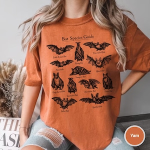May include: Orange short-sleeved t-shirt featuring a black graphic of various bat species with the text "Bat Species Guide". The shirt is a relaxed fit and made of a soft material.