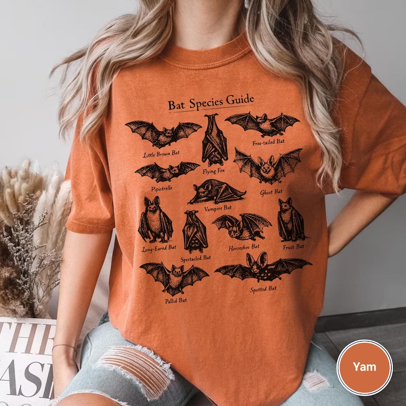May include: Orange short-sleeved t-shirt featuring a black graphic of various bat species with the text "Bat Species Guide". The shirt is a relaxed fit and made of a soft material.