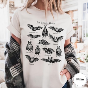 May include: White t-shirt featuring a black and white illustration of various bat species, including Little Brown Bat and Flying Fox, with the text "Bat Species Guide". The shirt is a casual, everyday wear item.