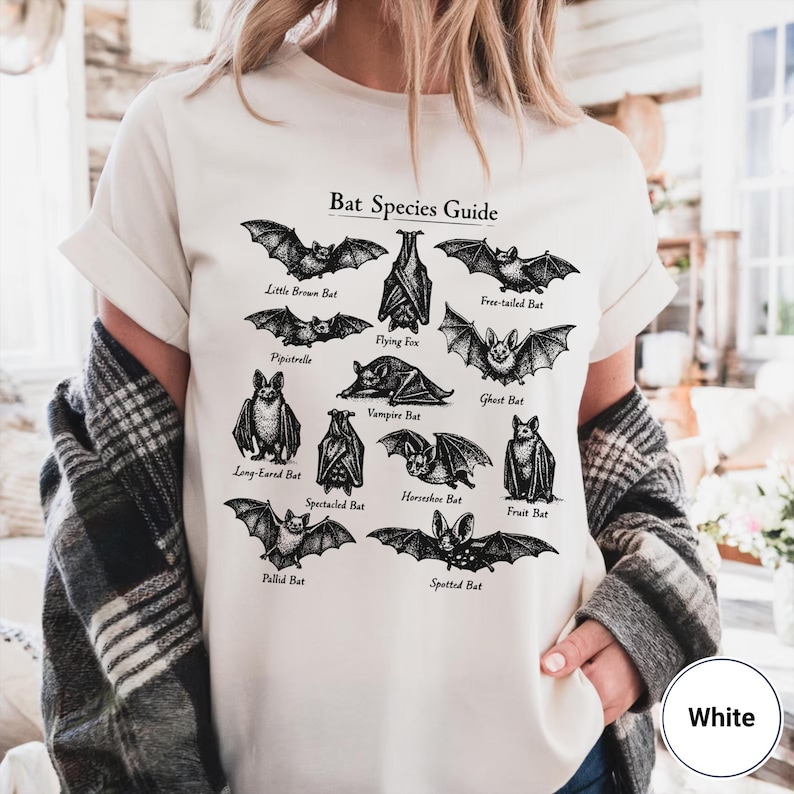 May include: White t-shirt featuring a black and white illustration of various bat species, including Little Brown Bat and Flying Fox, with the text "Bat Species Guide". The shirt is a casual, everyday wear item.