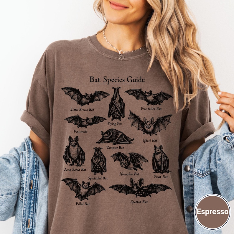 May include: Espresso-colored t-shirt featuring a detailed "Bat Species Guide" graphic. The design includes various bat illustrations with their names, such as "Little Brown Bat" and "Flying Fox". The shirt has a relaxed fit.