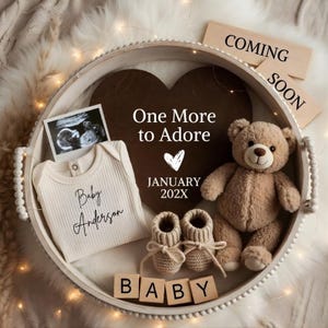 May include: A baby announcement scene with a round tray holding a wooden heart and a teddy bear. The tray contains a baby onesie with the name "Baby Anderson", baby booties, and a sonogram photo. The words "One More to Adore", "January 202X", "Coming Soon", and "BABY" are also displayed.