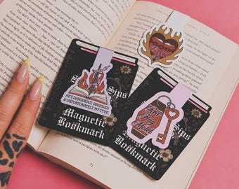 May include: Three magnetic bookmarks featuring illustrated designs. One shows an open book with a sword and flames, reading HE'S DANGEROUS, OBSESSED & UNFORTUNATELY MY TYPE. Another depicts a heart with flames and the text Locked In. The third shows a Red Flag Motel keychain.