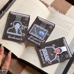 May include: Three rectangular magnetic bookmarks with dark floral backgrounds. One features a character illustration with the text 'This is the skin of a killer, Bella', another shows a 'The City of Forks Welcomes You' sign, and the third displays a character with the text 'Daddy'.